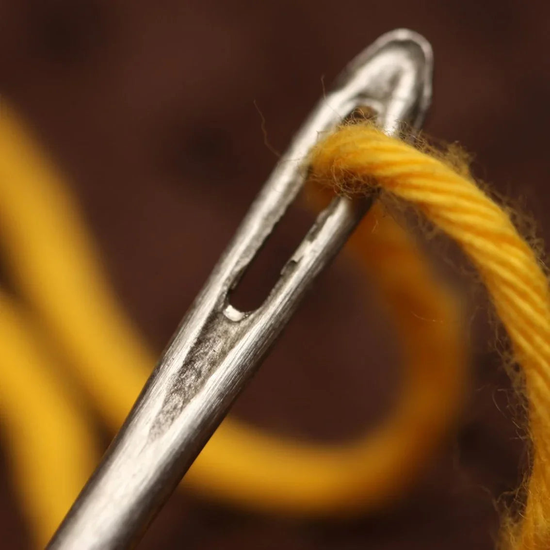 Close-up of a needle threaded with yellow yarn, emphasizing needlework and embroidery.