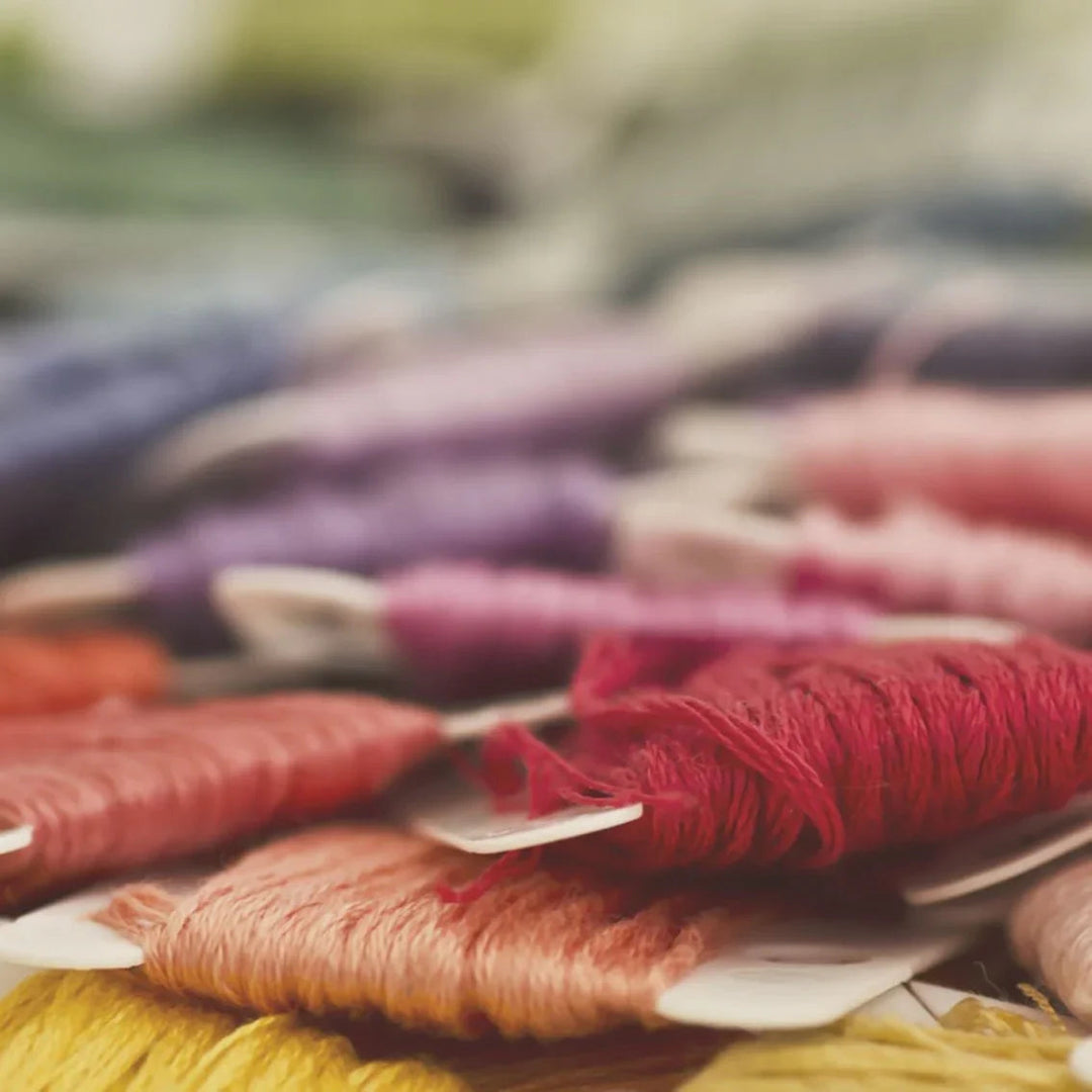 Colorful embroidery threads in shades of red, pink, purple, and yellow arranged closely.