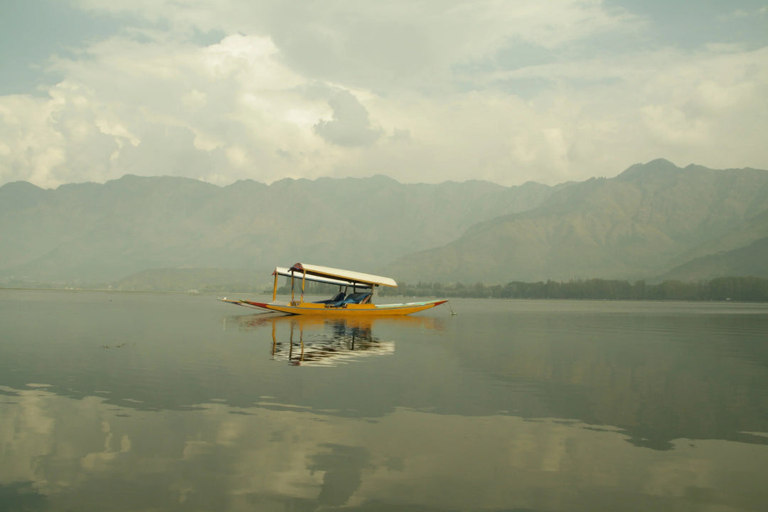 Wooden shikara boat floating on Dal Lake with mountains in the background, Kashmir